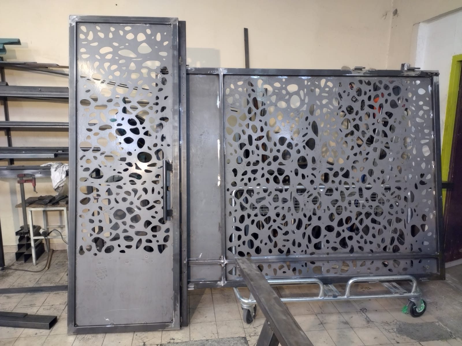 Portail et portillon à tôle découpée en acier brut, sur un chariot dans l’atelier, avant finition