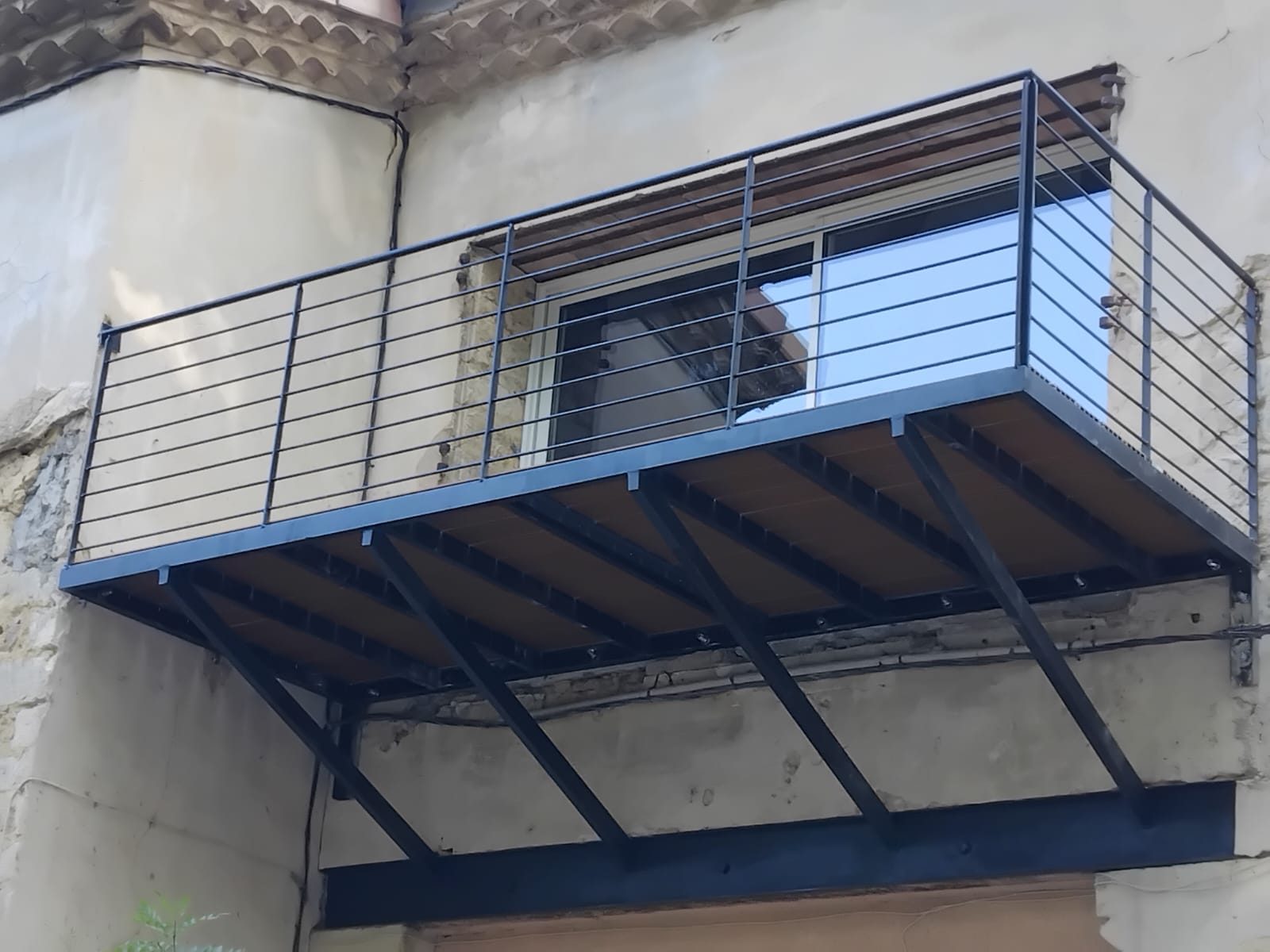 Balcon en acier en console sur une façade ancienne, jambes de force et garde-corps à lisses horizontales