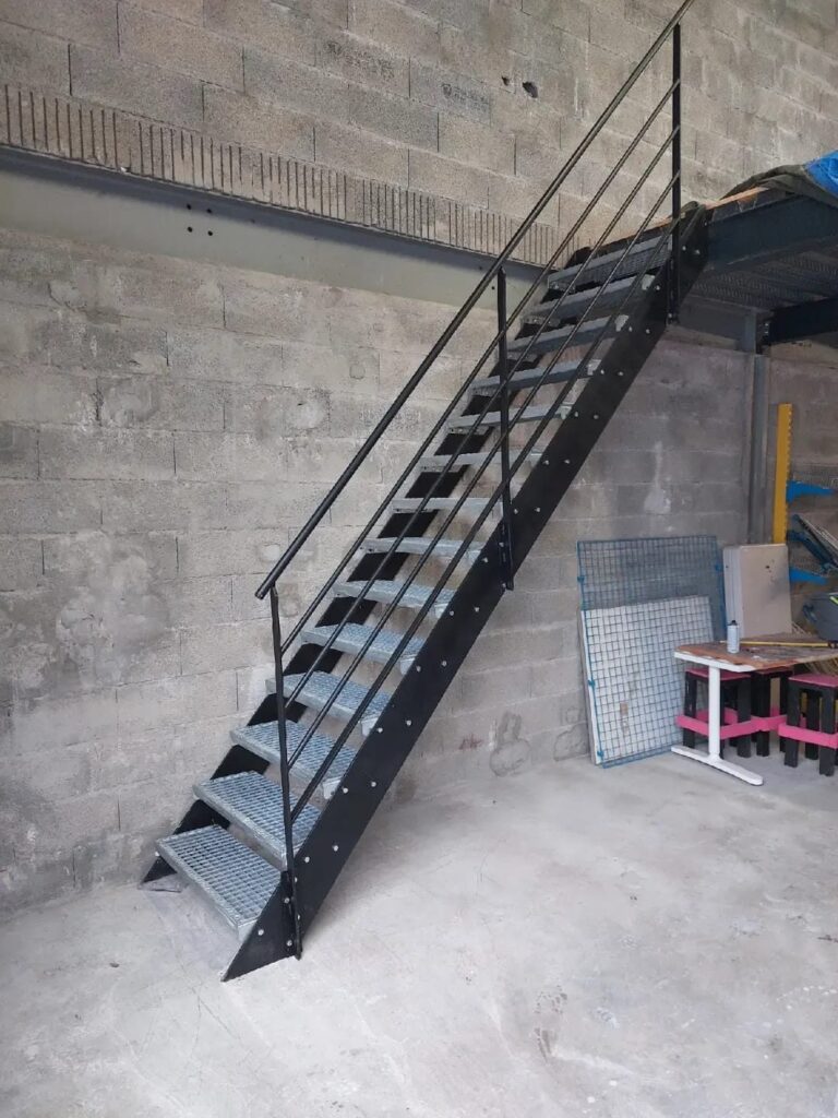 Escalier droit en acier noir à marches en caillebotis, accès à une mezzanine