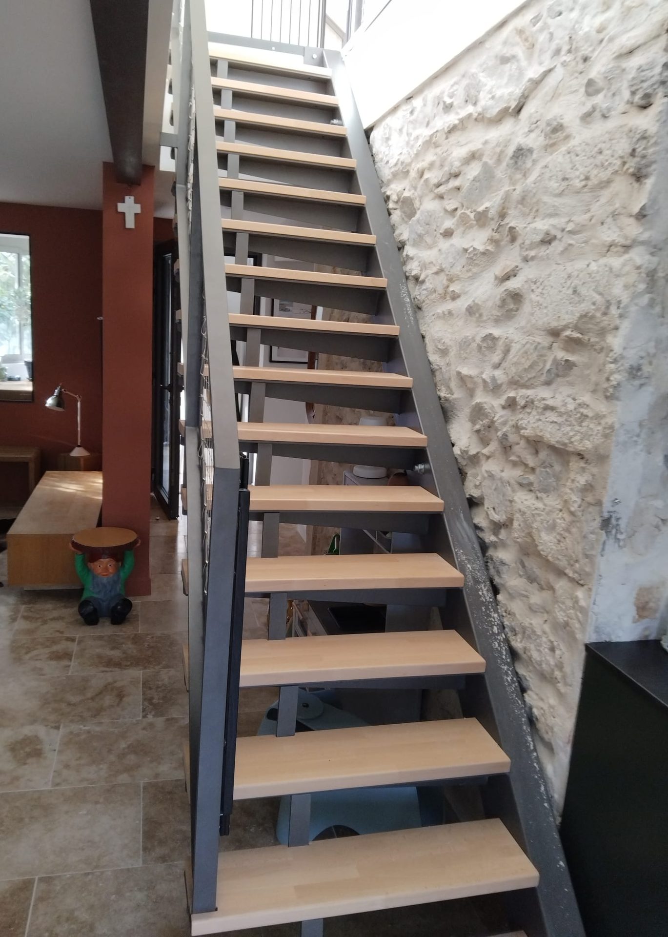 Escalier droit à limons en acier anthracite et marches en bois clair, le long d’un mur en pierre