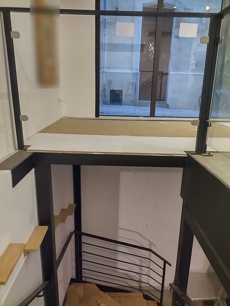 Mezzanine en acier d’un local commercial, garde-corps en verre à pinces sur poteaux acier