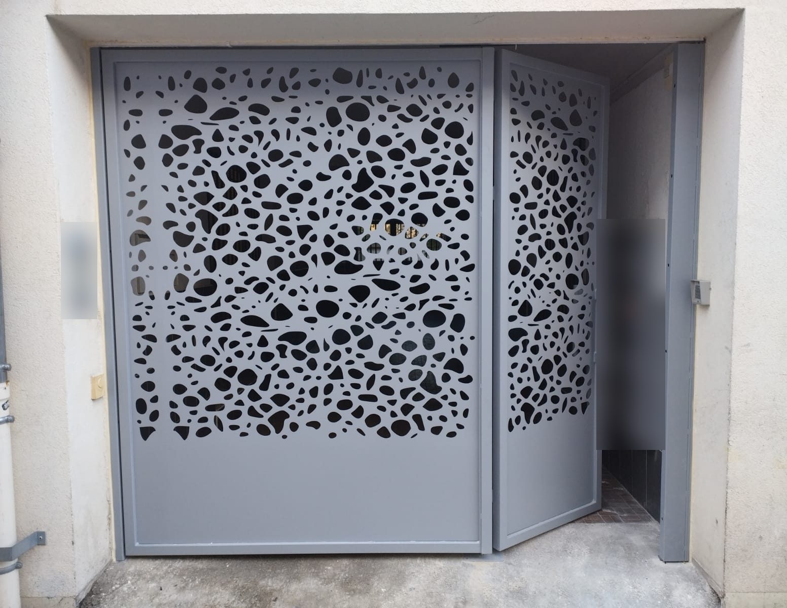 Portail d’entrée d’immeuble gris à tôle découpée, motif galets