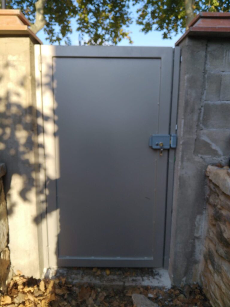 Portillon plein gris avec serrure en applique, entre deux piliers
