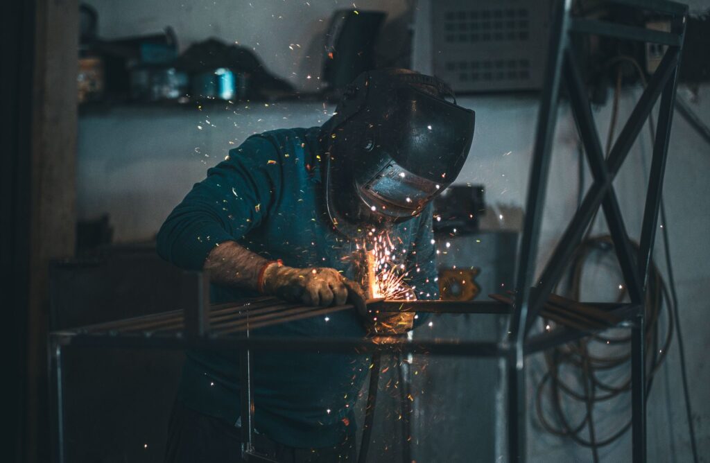 Photo d’illustration : soudeur casqué assemblant un cadre en acier, projection d’étincelles