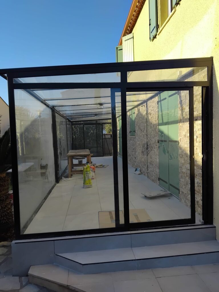Terrasse fermée à cadre acier noir, parois et toit vitrés, porte coulissante